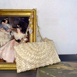 Detailed view of woven straw envelope bag with pearl and seashell chain strap decor