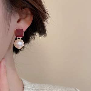 Close-up of vintage gold earrings with burgundy enamel and pearl drop on model ear