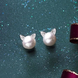 Detail of silver cat-ear pearl stud earrings on a dark green textured backdrop