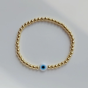 Detail of gold beaded bracelet with a blue evil eye charm on a white background