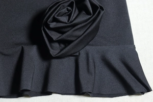 Detailed close-up of a 3D rose flower ornament and ruffled hem on a black bodycon dress