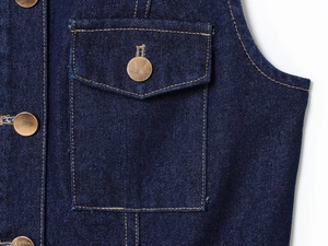 Close-up of dark blue denim fabric with gold metal buttons and contrast stitching