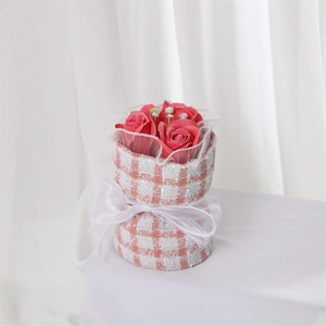 Pink soap rose bouquet in pink and white tweed wrap with a white ribbon bow on white base