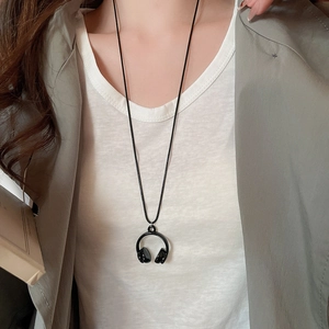 Detail of a minimalist black headphone pendant necklace worn on a white shirt and blazer