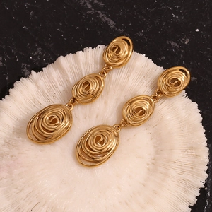 Détail macro de boucles d'oreilles pendantes à triple spirale dorée et texture martelée