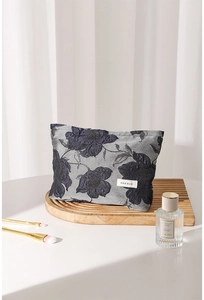 Detail of dark blue floral jacquard cosmetic bag with H&R BAG label on a wooden surface