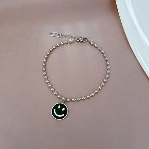 Nahaufnahme der Silberperlenkette mit grünem Smiley-Anhänger auf beigem Hintergrund