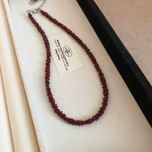 Macro shot of deep red crushed stone beads and metal chain on a white display tray