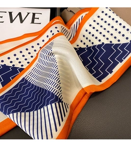 Detailed close-up of navy and white polka dot silk scarf with orange contrast piping
