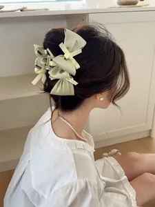 Detail view of model wearing a sweet light yellow bow hair claw clip with satin texture