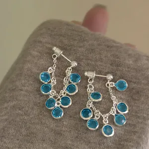 Detail of silver drop earrings featuring sky blue resin stones and flowing chain tassels