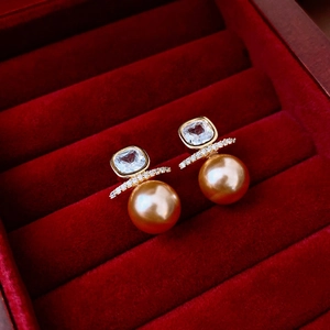 Detail of square zircon earrings with golden pearl in a red velvet jewelry box