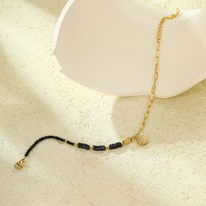 Detail of beaded gold chain bracelet with black stone charms and sun motif pendant