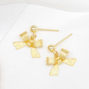 Pair of gold plated matte bow earrings on white fabric background, professional still life photo