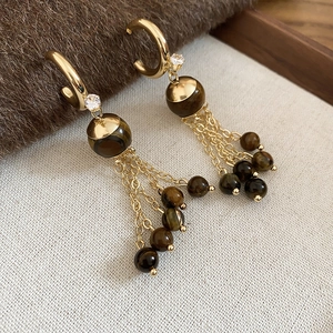 Detail of C-shaped golden earrings with brown tiger eye beads and delicate tassels
