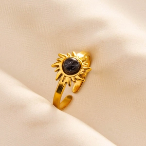 Macro shot of gold sunburst ring with black marble stone on silk fabric background
