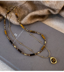 Detail of layered gold necklace with tiger eye stones on blue book and camel knitwear