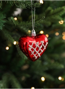 Close-up of red heart Christmas ornament with white glitter patterns on festive tree