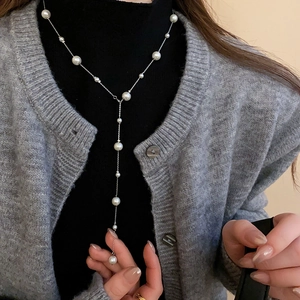 Silver Y-shaped faux pearl necklace on black sweater showing French luxury aesthetic