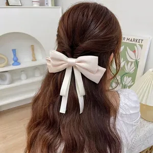 Creamy white satin bow hair clip with long ribbons worn by a model in a cozy setting