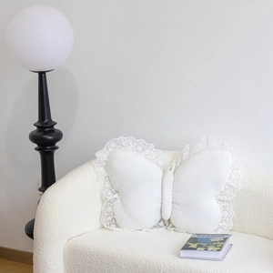 Detail of white butterfly decorative pillow with lace trim on a modern white fleece sofa