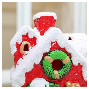 Detail of a red ceramic Christmas house with thick faux snow and green wreath decorations