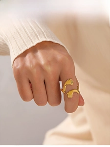 Detail of gold-plated stainless steel hugging hands ring worn on a finger