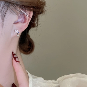Close-up of heart-shaped zircon stud earring with blue gem on ear for woman