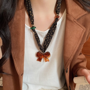 Detail of fabric bow necklace with amber acrylic pendant on polka dot scarf chain