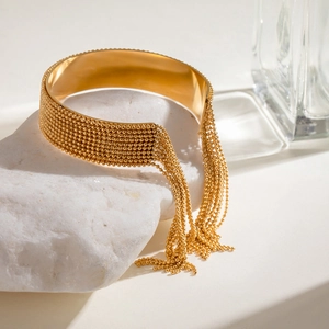 Dettaglio del bracciale rigido dorato con frange di perline metalliche su pietra bianca