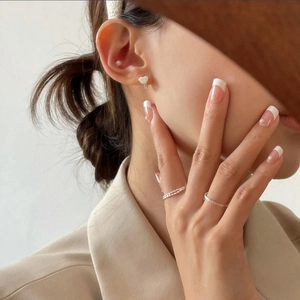 Close-up of 925 silver heart earring and minimalist rings on a model with neutral tones