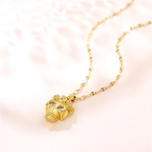 Gold skull pendant necklace with crown and sparkling zircon crystals on pink background