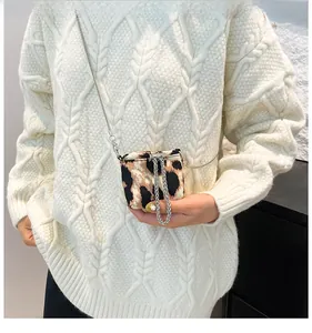 Close-up of leopard print mini crossbody bag with silver chain strap on knit sweater