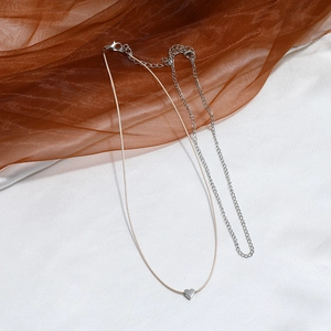 Detail of a minimalist double-layered necklace with a beige cord and silver heart pendant