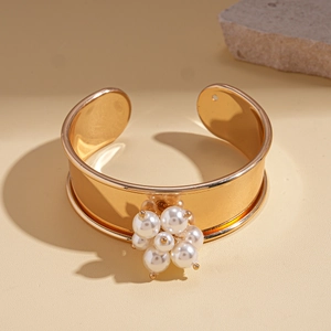 Detailed shot of open golden bangle featuring elegant white pearl cluster on almond background