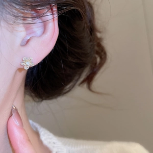 Close-up of elegant gold flower stud earrings with sparkling zircon crystals on ear