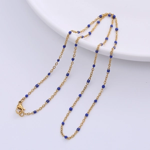 Minimalist golden O-chain necklace featuring small blue beads on a white ceramic tray