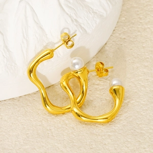 Macro shot of 18k gold wave-shaped earrings with round white pearls on a stone prop