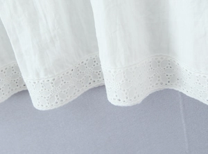 Dettaglio del tessuto in cotone bianco con ricami in pizzo floreale e consistenza