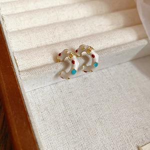 Macro shot of French style C-shape earrings with colorful enamel dots on linen padding