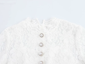 Détail d'une robe en dentelle blanche avec boutons de perles et bordure dorée chic