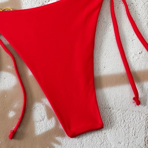 Detailed close-up of red bikini bottom featuring side ties and golden ring hardware