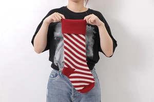 Detail of red and white striped knit Christmas stocking held by hand on white backdrop