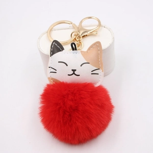 Close-up of a cute cat plush keychain featuring a red pom pom and gold lobster clasp