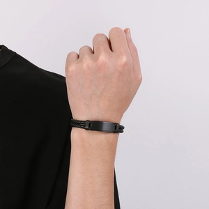 Détail d'un bracelet en cuir tressé pour homme avec plaque en métal noir mat au poignet