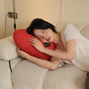 Cozy red heart shaped pillow held by model on a beige sofa in a minimalist home