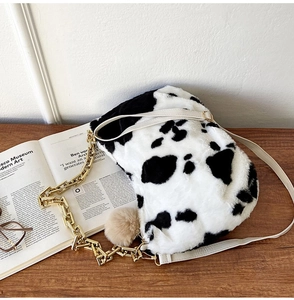 Detail of plush cow print tote bag featuring a gold metal chain and soft pom-pom charm