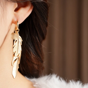 Detail view of gold feather drop earrings with sparkling zircon and frosted bead decor