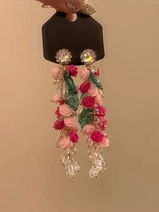 Detail of pink and red flower tassel earrings with green leaves on a display card