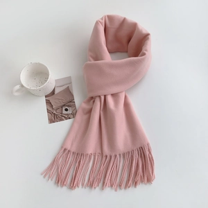 Close-up of a soft pink cashmere-like scarf with fringe tassels on a clean white desk